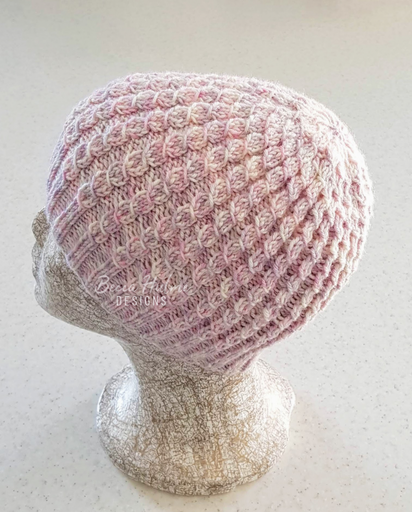 Mottled pink beanie-style knitted hat on a headform.